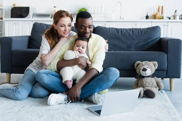 Joyeuse famille multiethnique regarder un film sur ordinateur portable tout en étant assis sur le sol — Photo de stock