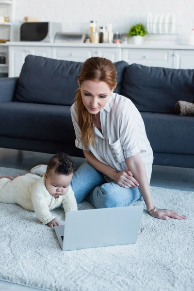 Mother sitting on floor near african american baby girl and laptop — Stock Photo