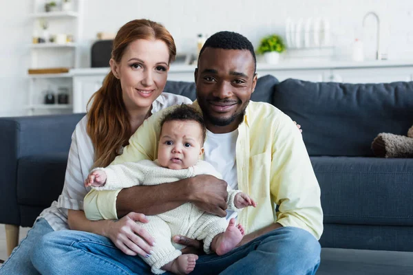 Joyful interracial couple with infant child smiling at camera — Stock Photo