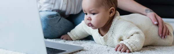 African american baby girl on floor near laptop and mother, banner — Stock Photo
