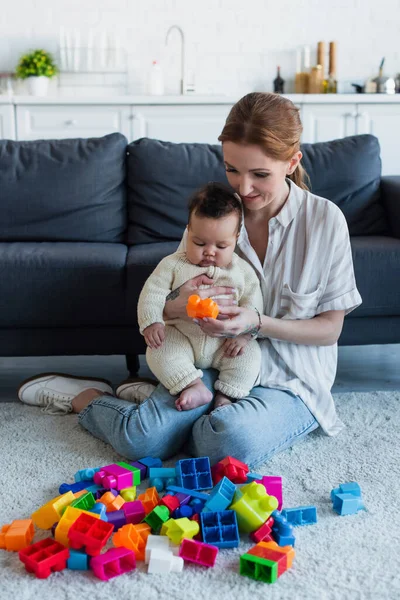 Mulher sentada no chão com a menina americana africana infantil perto de blocos de construção multicoloridos — Fotografia de Stock