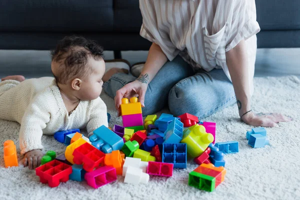 African american baby girl crawling on floor near mother and colorful building blocks — Stock Photo