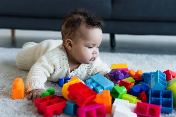 Bambino africano americano in pagliaccetto a maglia sul pavimento vicino a blocchi di costruzione multicolore — Foto stock