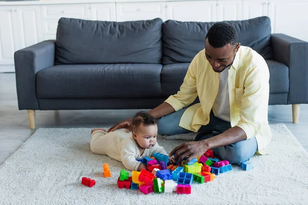 Afro-américain homme jouer avec bébé fille et blocs de construction colorés sur le sol à la maison — Photo de stock