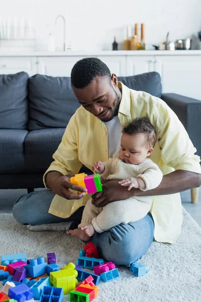 Afro-americano pai brincando com bebê e blocos de construção multicoloridos no chão em casa — Fotografia de Stock