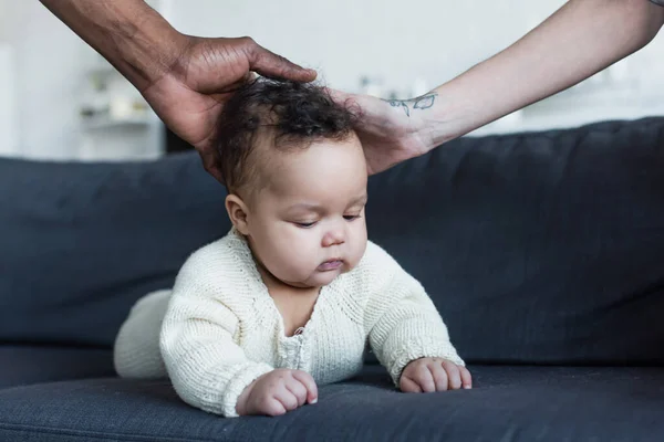Multiethnic parents touching head of african american baby crawling on sofa — Stock Photo