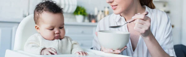 Donna che dà da mangiare al piccolo bambino afroamericano con colazione, striscione — Foto stock