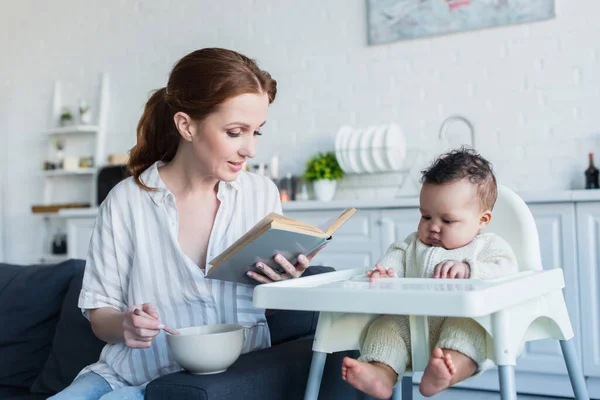 Mother reading book to african american baby girl during breakfast — Stock Photo