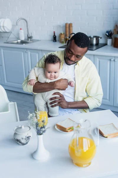 Homem americano africano sentado com a filha infantil perto da mesa com café da manhã — Fotografia de Stock