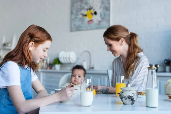 Preteen menina tomando café da manhã perto de mãe e bebê afro-americana irmã — Fotografia de Stock