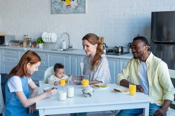 Familia multiétnica sonriente desayunando en la cocina - foto de stock