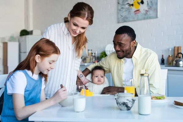 Feliz familia multiétnica sonriendo durante el desayuno en la cocina - foto de stock