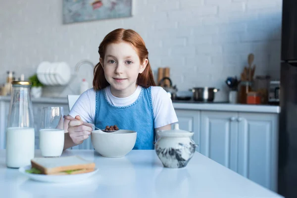 Lächelndes Mädchen, das in die Kamera schaut, während es knusprige Cornflakes isst — Stockfoto