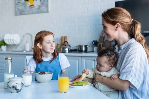 Mujer feliz desayunando con hijas multiétnicas en la cocina - foto de stock