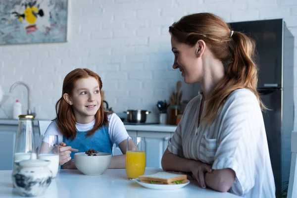 Glücklich rothaarige Mädchen im Gespräch mit lächelnder Mutter während des Frühstücks — Stockfoto