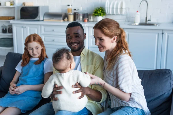 Feliz afroamericano hombre sosteniendo infante niño cerca sonriente multiétnica familia - foto de stock