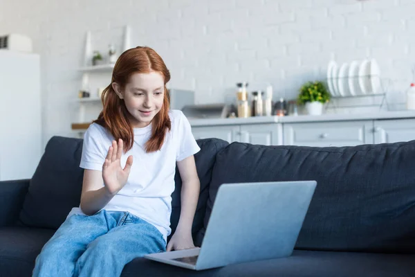 Sorridente ragazza mano agitando durante la videochiamata sul divano — Foto stock