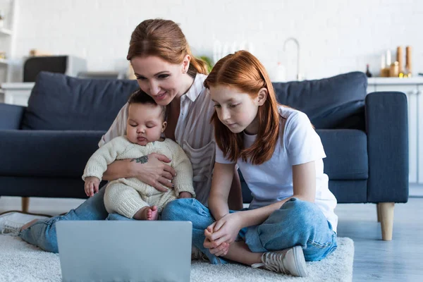 Mère heureuse avec des filles multiethniques regarder un film sur ordinateur portable à la maison — Photo de stock