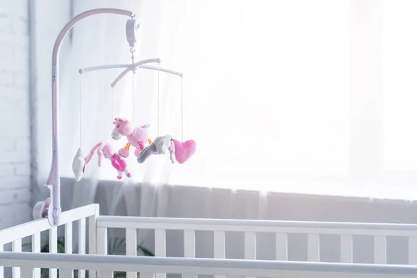 Soft toys hanging over crib in nursery near window — Stock Photo