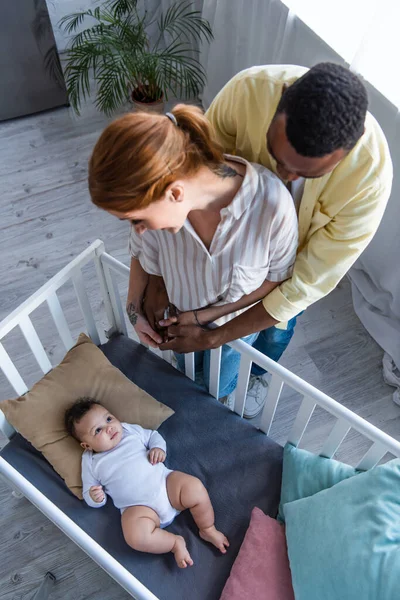 Вид зверху на афроамериканця, який обіймає дружину біля немовляти, лежачи в ліжечку — стокове фото