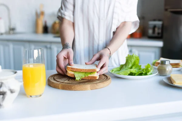 Vista recortada de la mujer sosteniendo sándwich mientras prepara el desayuno - foto de stock