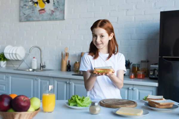 Ruiva preteen menina segurando saboroso sanduíche na cozinha — Fotografia de Stock