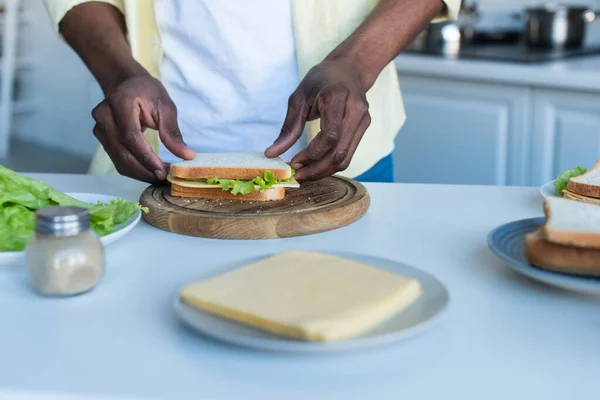 Teilansicht eines afrikanisch-amerikanischen Mannes, der Sandwich zum Frühstück macht — Stockfoto