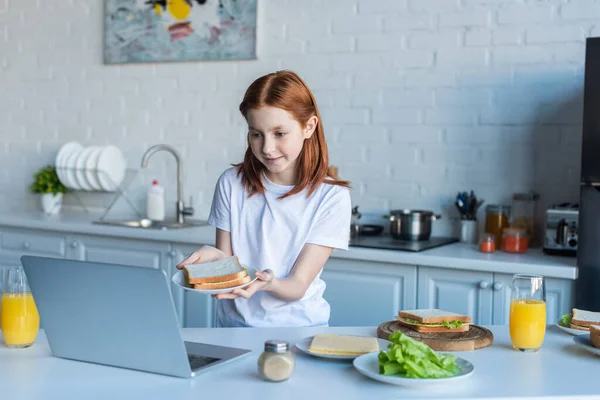 Дитина показує сендвіч під час відеодзвінка на ноутбук на кухні — Stock Photo