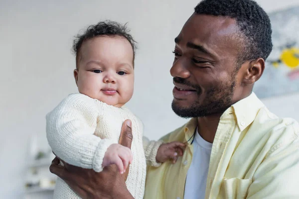 Cheerful african american man holding smiling infant daughter — Stock Photo