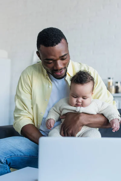 Afrikanisch-amerikanischer Mann hält Mädchen in der Nähe von verschwommenem Laptop — Stockfoto