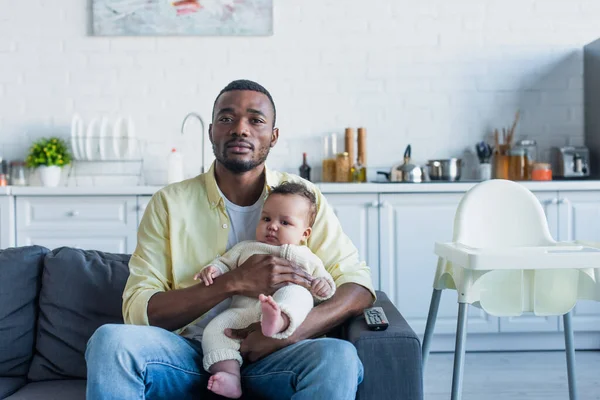 Africano americano homem assistindo tv na cozinha com bebê menina — Fotografia de Stock