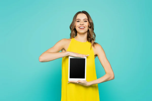Усміхнена жінка показує цифровий планшет з порожнім екраном ізольовано на синьому — стокове фото