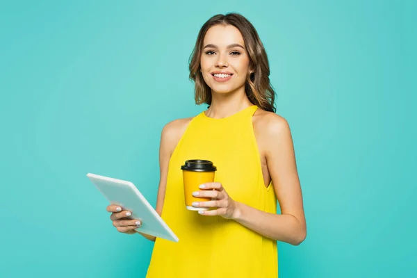 Hübsch lächelnde Frau mit Pappbecher und digitalem Tablet isoliert auf blau — Stockfoto