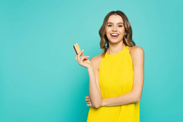 Bella donna sorridente alla fotocamera mentre tiene la carta di credito isolata sul blu — Foto stock