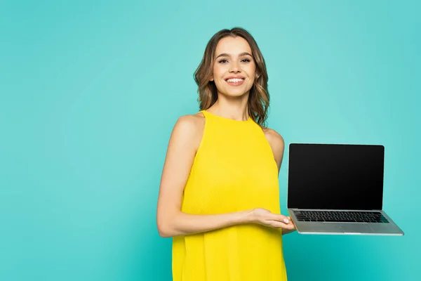 Fröhliche Frau hält Laptop in der Hand und blickt in die Kamera auf blauem Hintergrund — Stockfoto