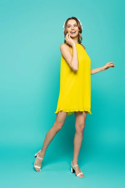 Femme souriante en robe et écouteurs sur fond bleu — Photo de stock