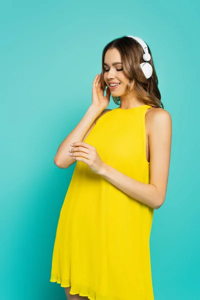 Donna sorridente in abito giallo utilizzando cuffie su sfondo blu — Foto stock