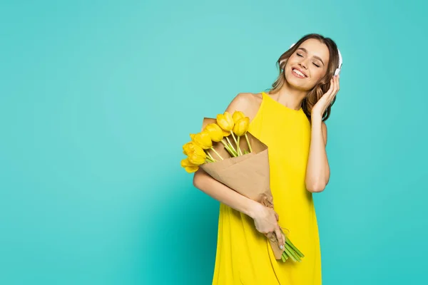 Улыбающаяся женщина в платье и наушниках с тюльпанами на синем фоне — стоковое фото