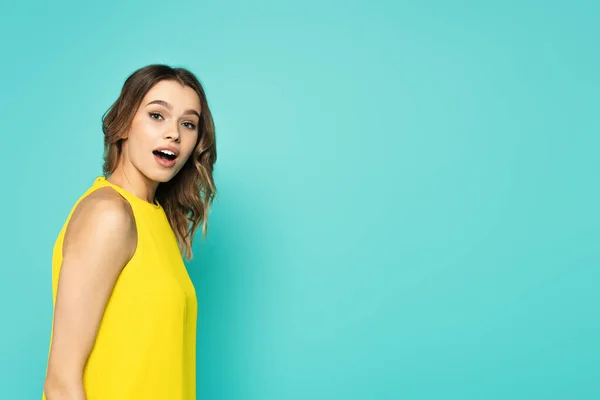 Astonished woman in yellow dress looking at camera isolated on blue — Stock Photo