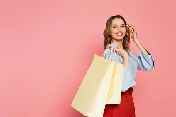 Mujer joven sosteniendo bolsas de compras y mirando hacia otro lado aislado en rosa - foto de stock