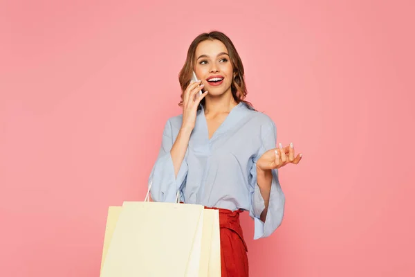 Mujer sonriente con bolsas de compras hablando en un smartphone aislado en rosa - foto de stock