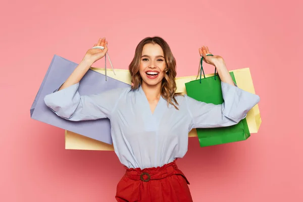Mulher alegre segurando sacos de compras coloridos no fundo rosa — Fotografia de Stock