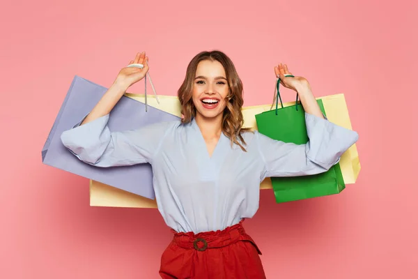 Femme gaie tenant des sacs à provisions colorés sur fond rose — Photo de stock