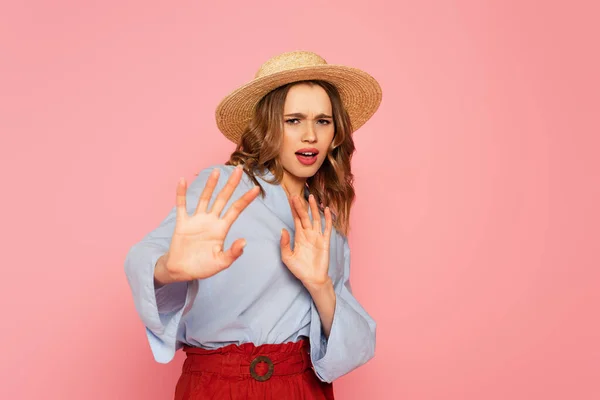 Offended woman in sun hat showing stop gesture isolated on pink — Stock Photo