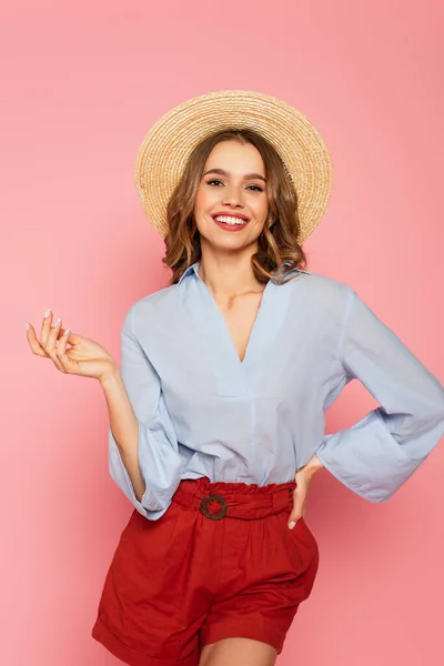 Stylish woman in sun hat smiling at camera and posing isolated on pink — Stock Photo