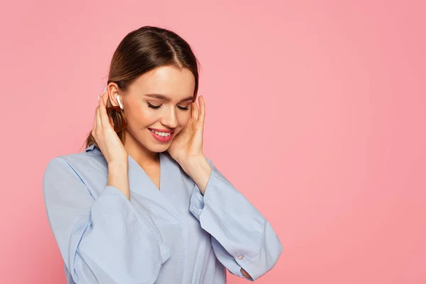 Bella donna sorridente mentre ascolta musica in auricolare isolato su rosa — Foto stock