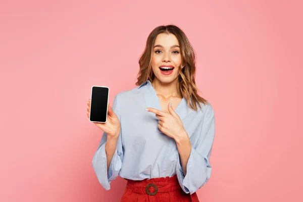 Femme excitée pointant vers le smartphone avec écran blanc sur fond rose — Photo de stock