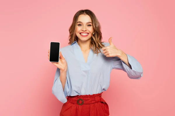 Elegante donna che mostra come e tenendo lo smartphone con schermo bianco su sfondo rosa — Foto stock