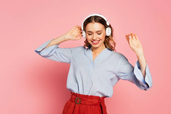 Femme positive dansant en écoutant de la musique dans un casque sur fond rose — Photo de stock