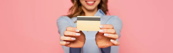 Vista recortada de la tarjeta de crédito en manos de una mujer borrosa aislada en rosa, pancarta - foto de stock